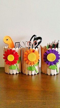 three small vases with paper flowers and scissors in them on a wooden table next to a white wall