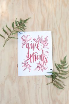 a card with the words give thanks written on it next to some green plant leaves