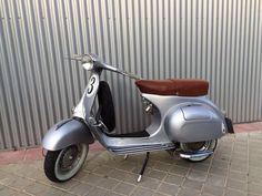 a silver scooter parked in front of a building with a brown leather seat