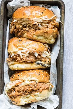 three pulled pork sandwiches sitting on top of each other in a baking pan with shredded parmesan cheese