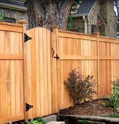 a wooden fence in front of a tree and some plants on the side of it