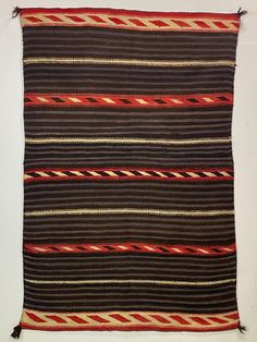 an old rug with red, black and brown stripes on the bottom is laying on a white surface