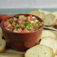 a red bowl filled with salsa next to crackers on a cutting board and tomatoes