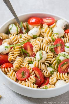 pasta salad with tomatoes, mozzarella and basil in a white bowl on a table