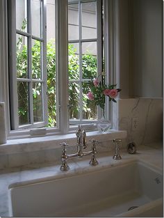 a white sink sitting under a window next to a vase with flowers in it on top of a counter