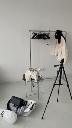 a camera and tripod in front of a white wall with clothes hanging on it