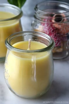 two jars filled with yellow candles sitting on top of a white counter next to each other