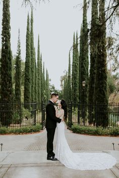 a bride and groom standing in front of an iron gate with trees behind them at their wedding