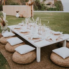 a table set up with place settings and white linens on the grass in front of an outdoor setting