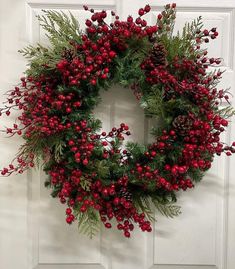 a wreath with red berries and greenery hanging on a door