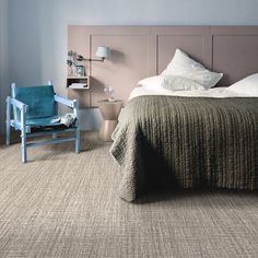 a bed sitting in a bedroom next to a blue chair and table on top of a carpeted floor