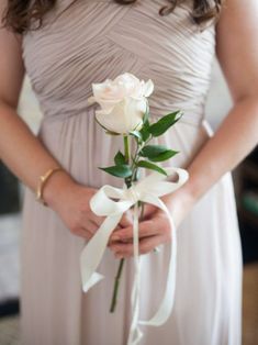 a woman in a dress holding a white rose and ribbon tied around her waist with both hands