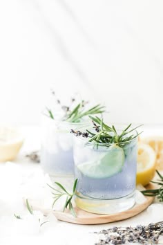 two glasses filled with lavender lemonade and rosemary garnish on a wooden tray