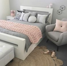 a bedroom with gray and pink decor, white bedding and grey chair in the corner