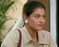 a woman with large earrings sitting in front of a plant and looking off into the distance