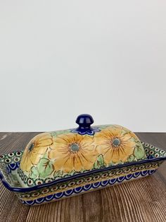 a yellow and blue flowered dish on a wooden table with a white wall in the background