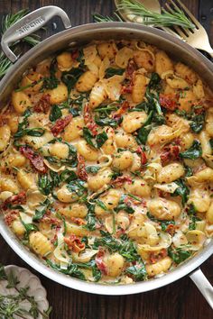 a pot filled with pasta and spinach on top of a wooden table next to utensils