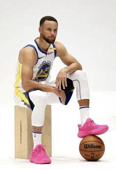 a basketball player sitting on top of a wooden block next to a pink nike shoe