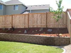 a wooden fence next to a brick wall and green grass in front of a house