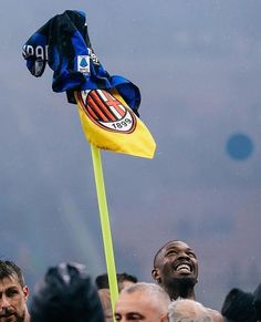 a group of people standing around each other and one person holding a yellow pole with a blue jacket on it