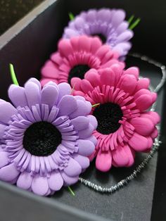 three purple and pink flowers are in a black box with silver wire on the bottom