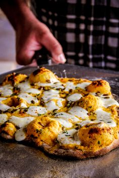 a person cutting up a pizza on top of a metal pan covered in cheese and toppings