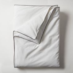 an unmade bed with white sheets and black piping on the bottom, along with two pillows