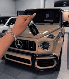 a person holding up a cell phone in front of a mercedes car at a dealership