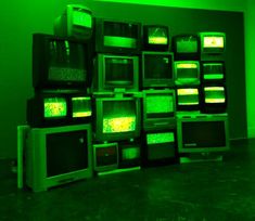 several televisions are stacked up in a room with green lights on the walls and floor