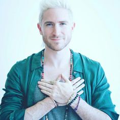 a man with white hair wearing a green jacket and beaded bracelets holding his hands together