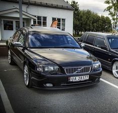 two cars parked in a parking lot next to each other near a house and trees