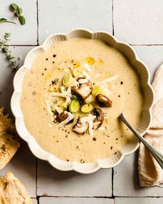 a white bowl filled with soup on top of a tiled floor next to bread slices