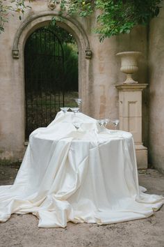 the table is covered with white cloths in front of an iron gate and tree