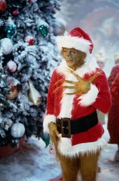 a monkey dressed as santa claus standing in front of a christmas tree with his hands on his chest