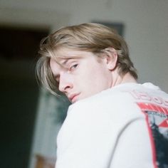 a young man wearing a white sweatshirt looking at the camera with his hand on his hip