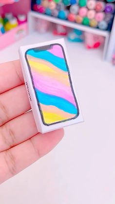 a hand holding a small box with a colorful design on the front and back of it