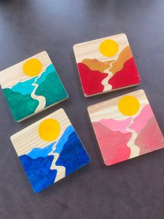 three wooden coasters with painted mountains and sun in the middle, on a table