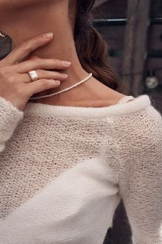 a woman wearing a white sweater with a diamond ring on her left hand and a necklace in the other hand