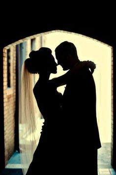 a bride and groom are silhouetted against an arch