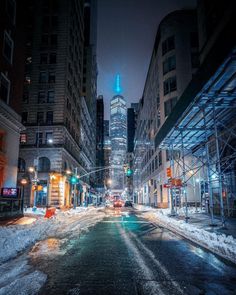 a city street at night with snow on the ground and tall buildings in the background