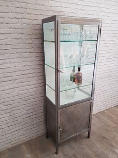 a glass display case with bottles and glasses in it next to a white brick wall