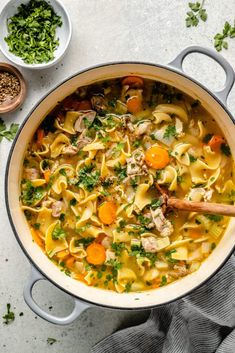 a pot filled with chicken noodle soup on top of a white table next to two bowls