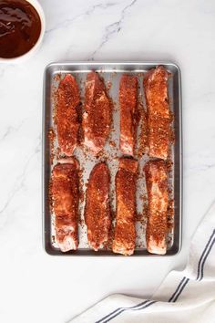 raw meat on a baking sheet next to dipping sauces and a white towel in the background