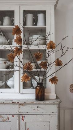 a vase filled with flowers sitting on top of a wooden table next to a white hutch