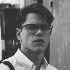 a young man wearing glasses standing in front of a building