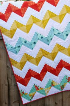 a colorful chevroned quilt hanging on a wooden fence