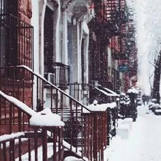 snow is falling on the sidewalk and stairs in front of an apartment building with wrought iron railings