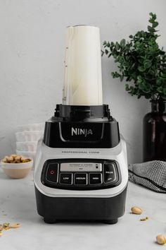 a blender sitting on top of a counter next to a bowl filled with nuts