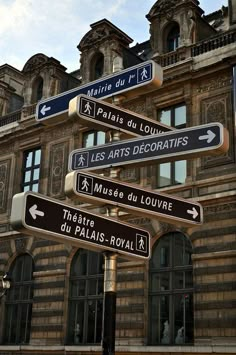 a street sign in front of a building with many windows and signs pointing to different locations