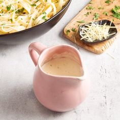 a pink pitcher filled with gravy next to a skillet of pasta and parmesan cheese